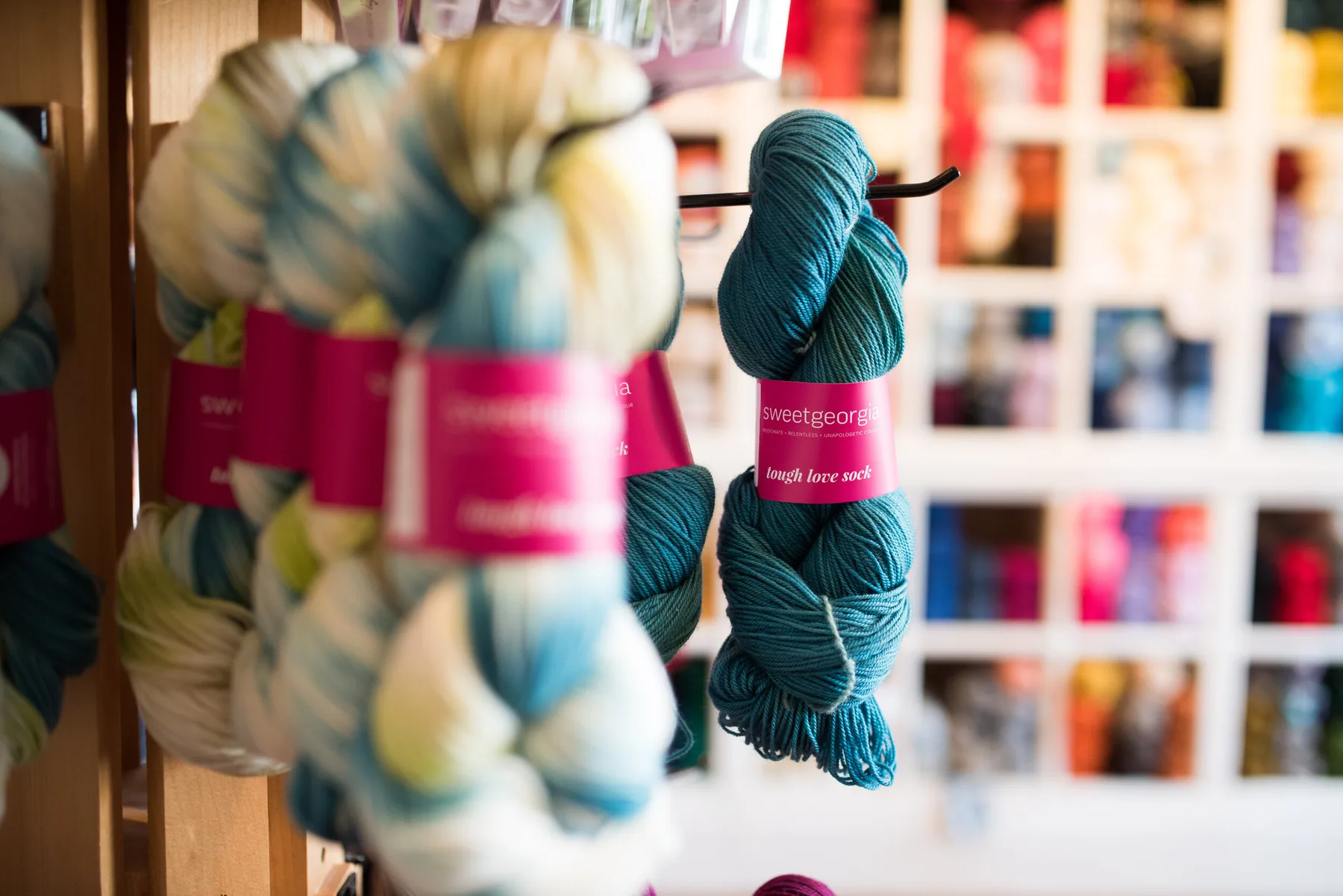 Teal and cream yarn displayed on wooden shelves at Wool On William